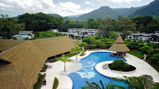A resort with a central swimming pool, thatched-roof structures, and lush greenery. - 4BR Private Pool Villa in Jacó | Ciudad del Mar #158 (Jacó)