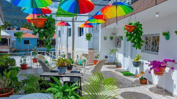 Una terraza en la azotea con jardineras colgantes, mobiliario exterior y vistas de la ciudad.