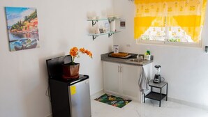 Una cocina compacta con refrigerador, lavamanos, una pequeña encimera y una ventana con cortinas amarillas.