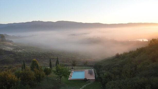 A pool area with a view of mist-covered hills and a clear sky. - The Lime Tree (Castiglion Ubertini)