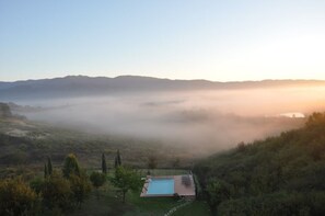 Un espace piscine offrant une vue sur des collines enveloppées de brume et un ciel dégagé.