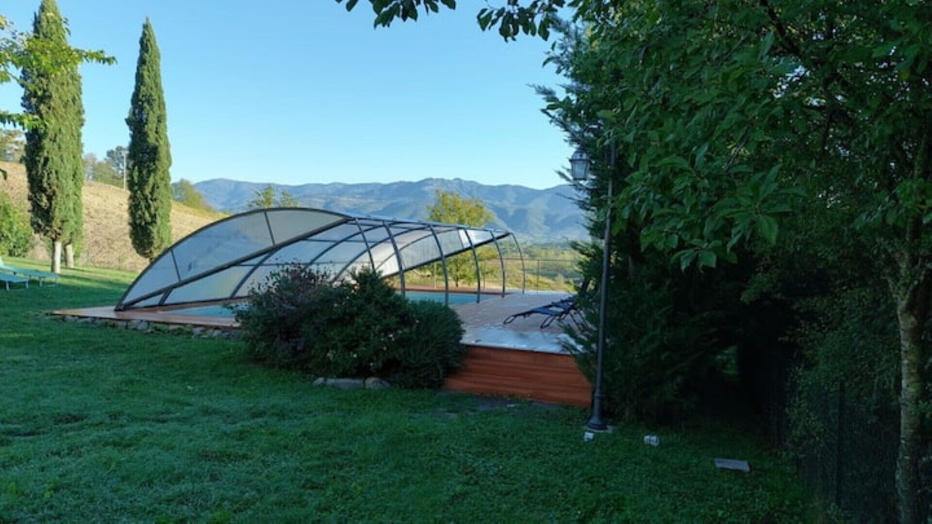 A greenhouse structure in a grassy area with a view of mountains in the background.