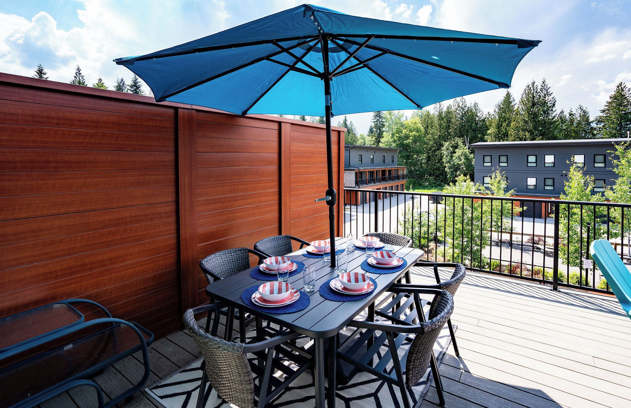A wooden deck with a table set for four, an umbrella, and a view of buildings in the background.
