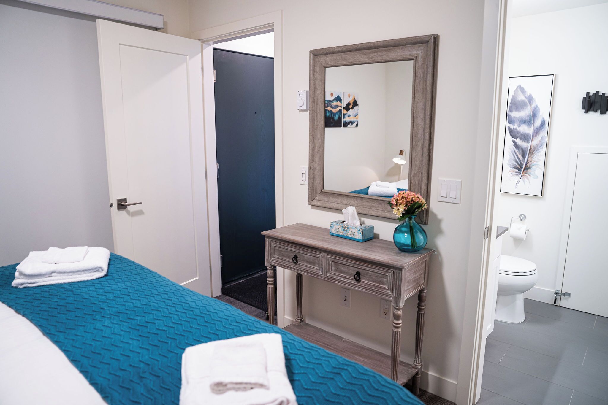 A hotel room with a bed, a dresser, a mirror, and a bathroom with a toilet and sink.