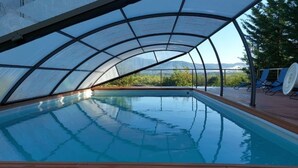 En swimmingpool med en glasvägg runt om, omgiven av solstolar och med utsikt över bergen.