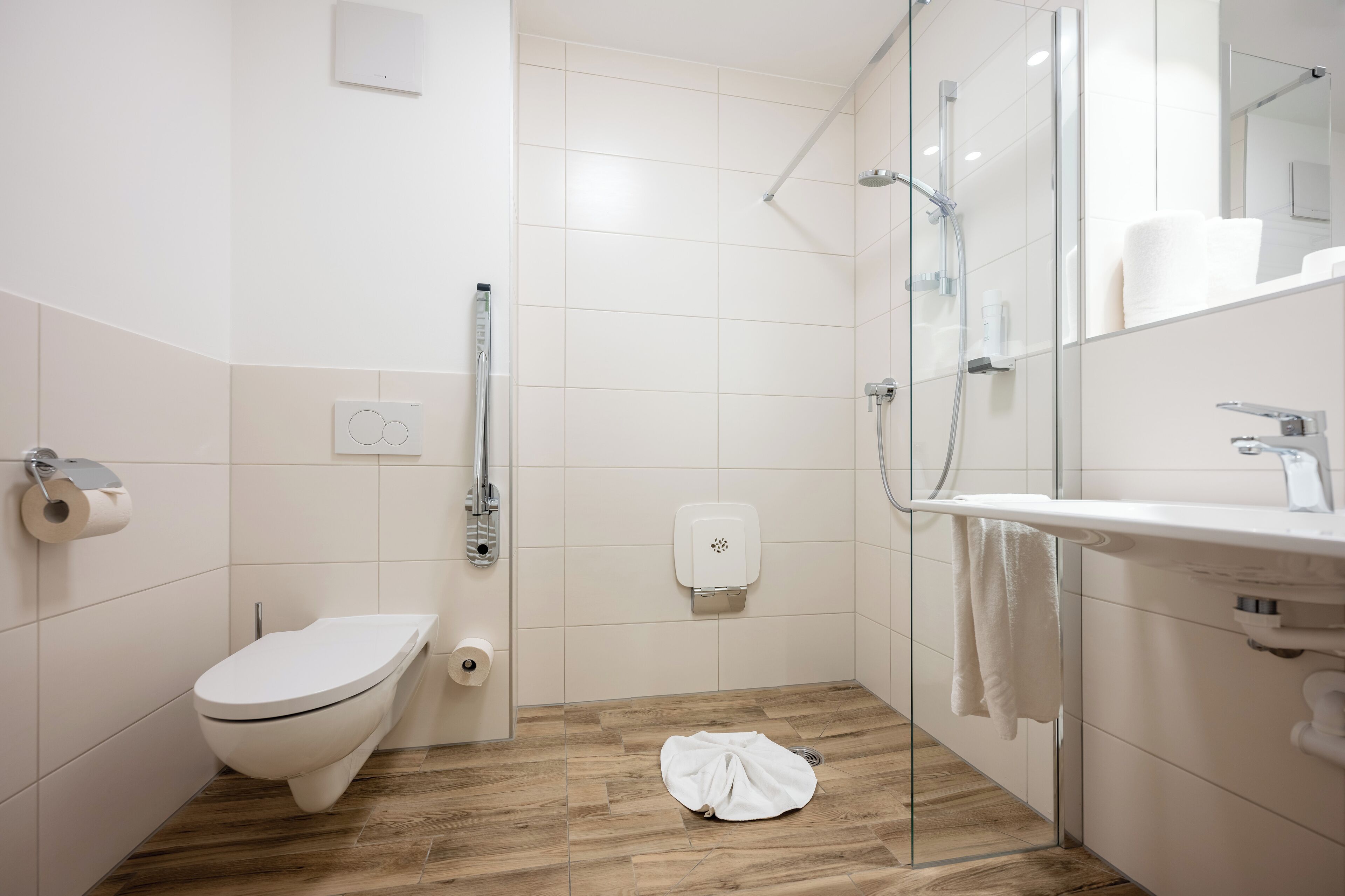 A modern bathroom with a toilet, a glass shower enclosure, a sink, and a towel rack.
