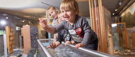 Kinder spielen mit Wasser in einem modernen Innenbereich mit Glasbarrieren und einer felsigen Landschaft im Hintergrund.