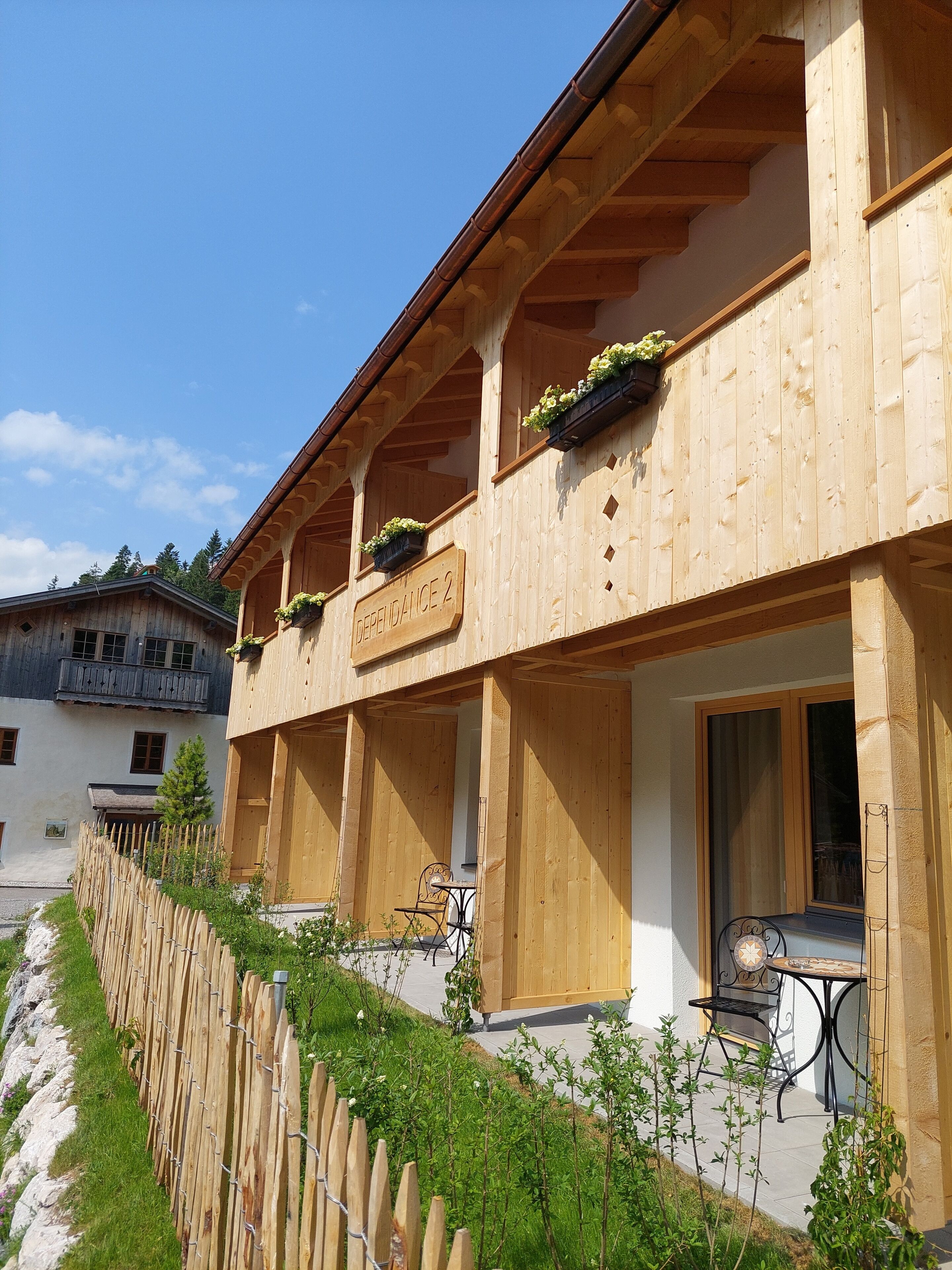 Un edificio de madera con balcones, un letrero que dice "DEPRENDANCE 2" y mobiliario exterior.