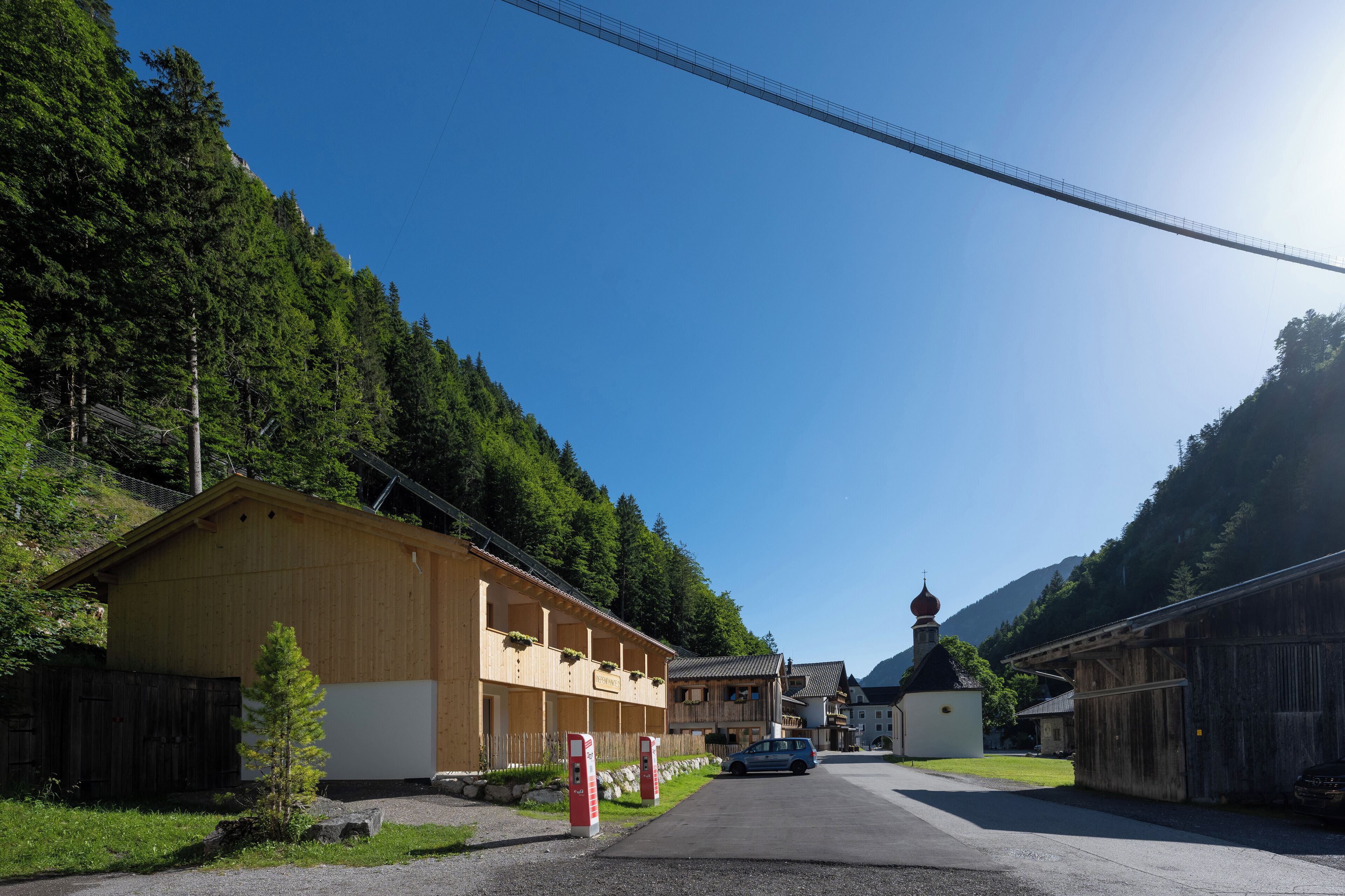 Une rue de campagne bordée de bâtiments en bois, avec une église et une voiture garée sur le côté.