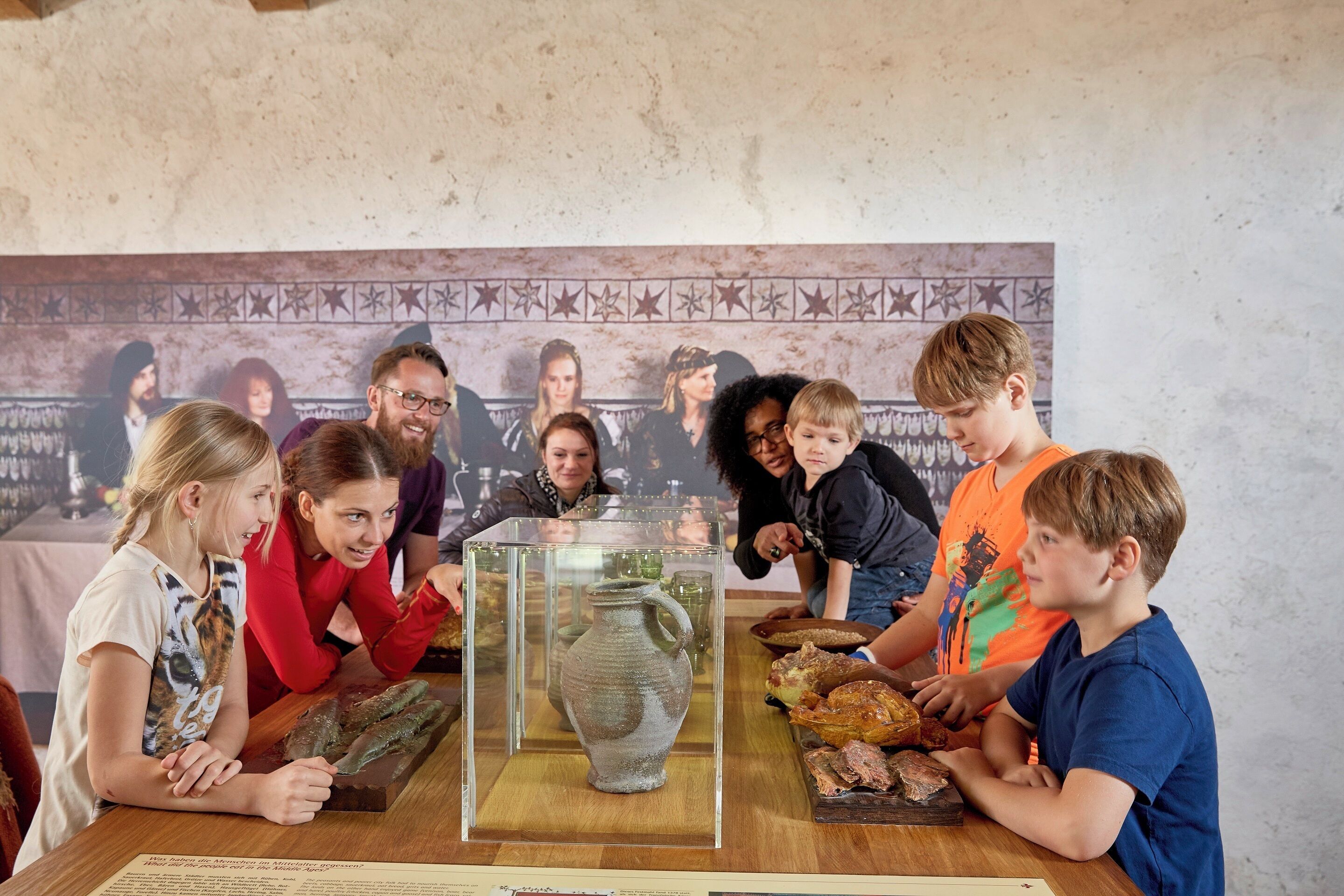 A group of people around a table with a display case containing a ceramic jug and various food items.