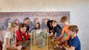 A group of people around a table with a display case containing a ceramic jug and various food items.