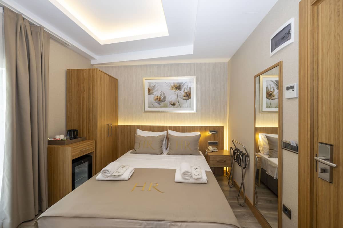 Habitación de hotel con cama, escritorio, espejo y cuadros en la pared.