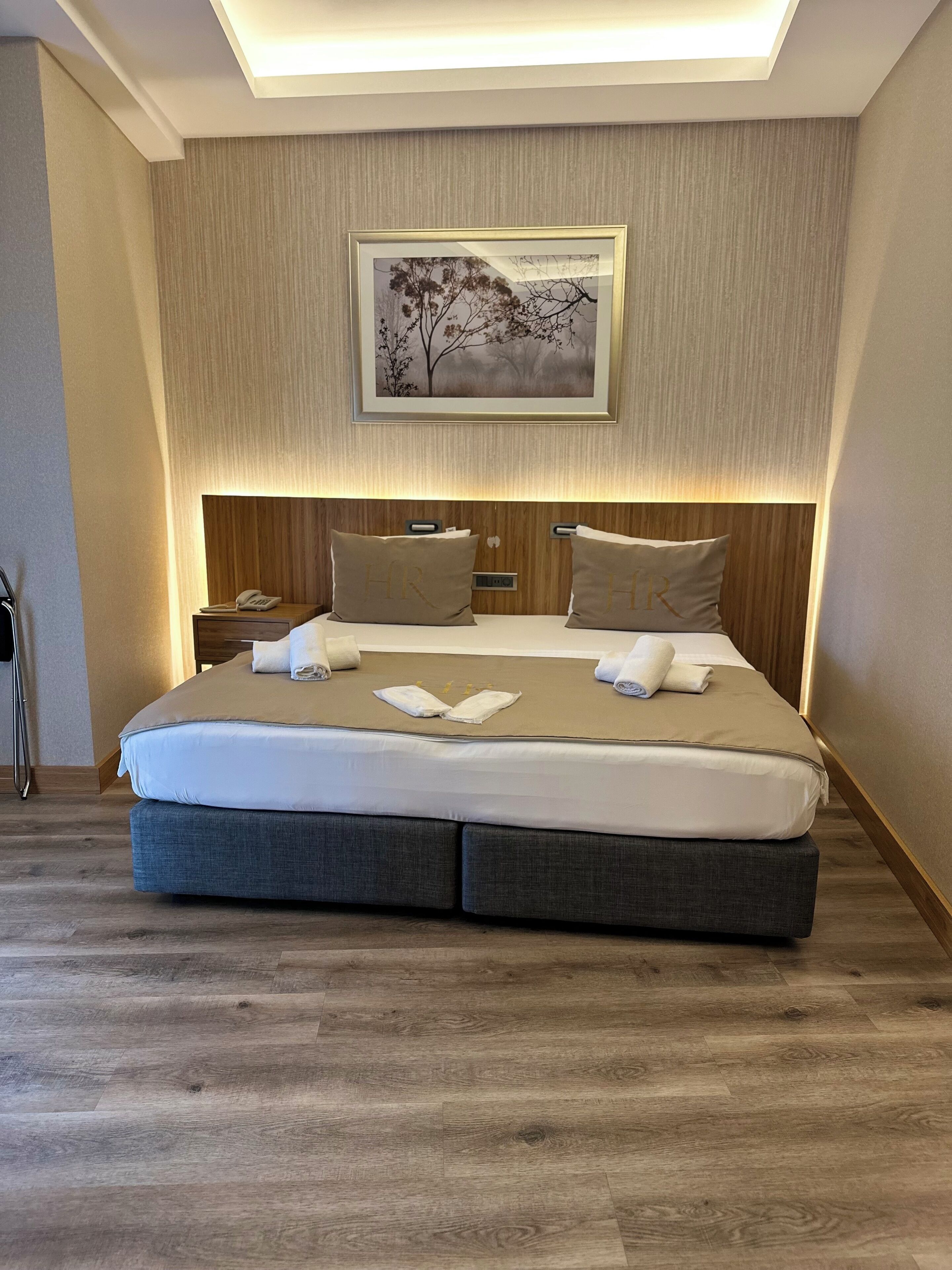 A modern hotel room with a large bed, wooden headboard, and a framed picture on the wall.