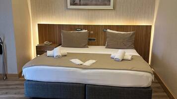 A modern hotel room with a large bed, wooden headboard, and a framed picture on the wall.