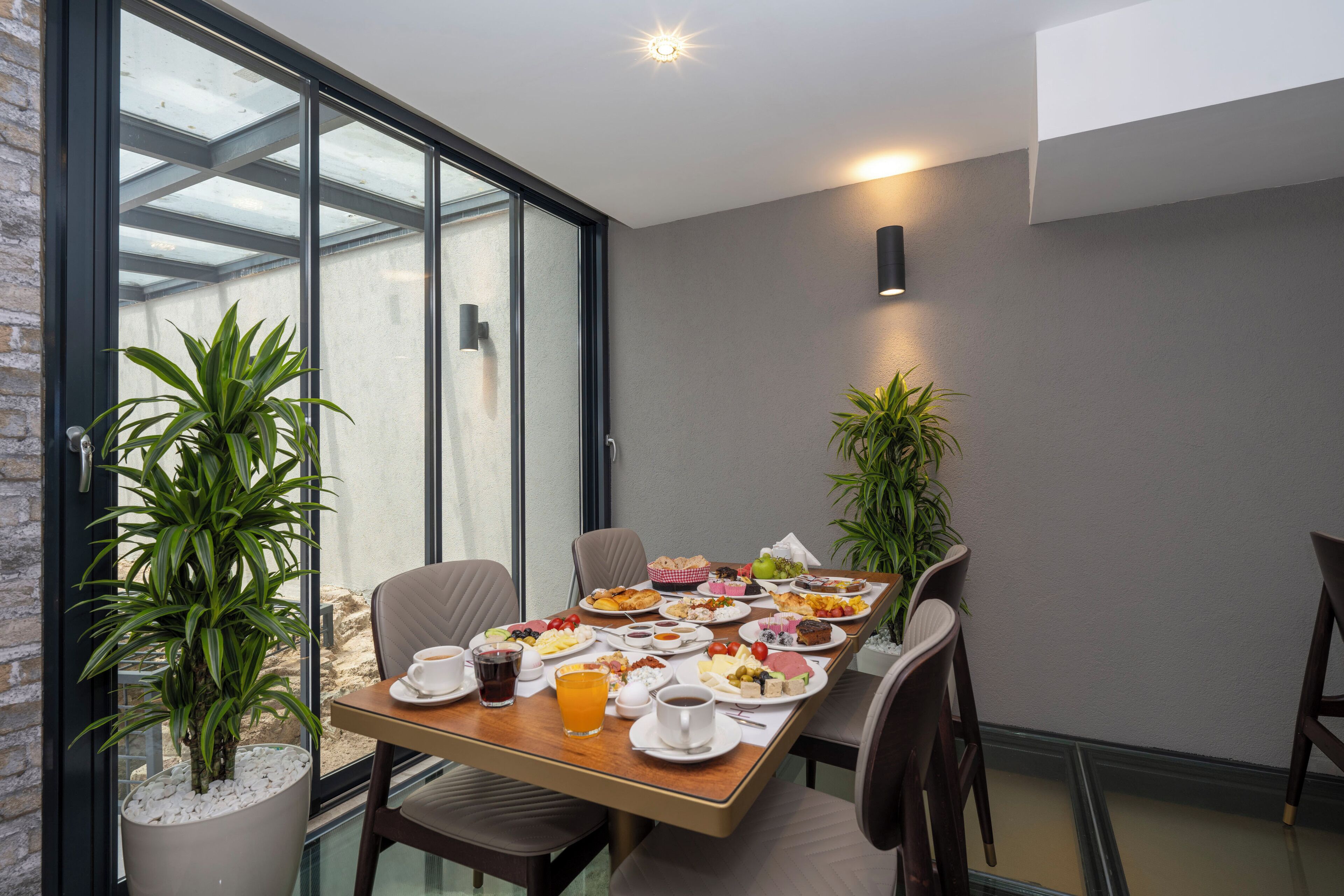 A dining area with a glass wall, modern furniture, and a variety of food and drinks.