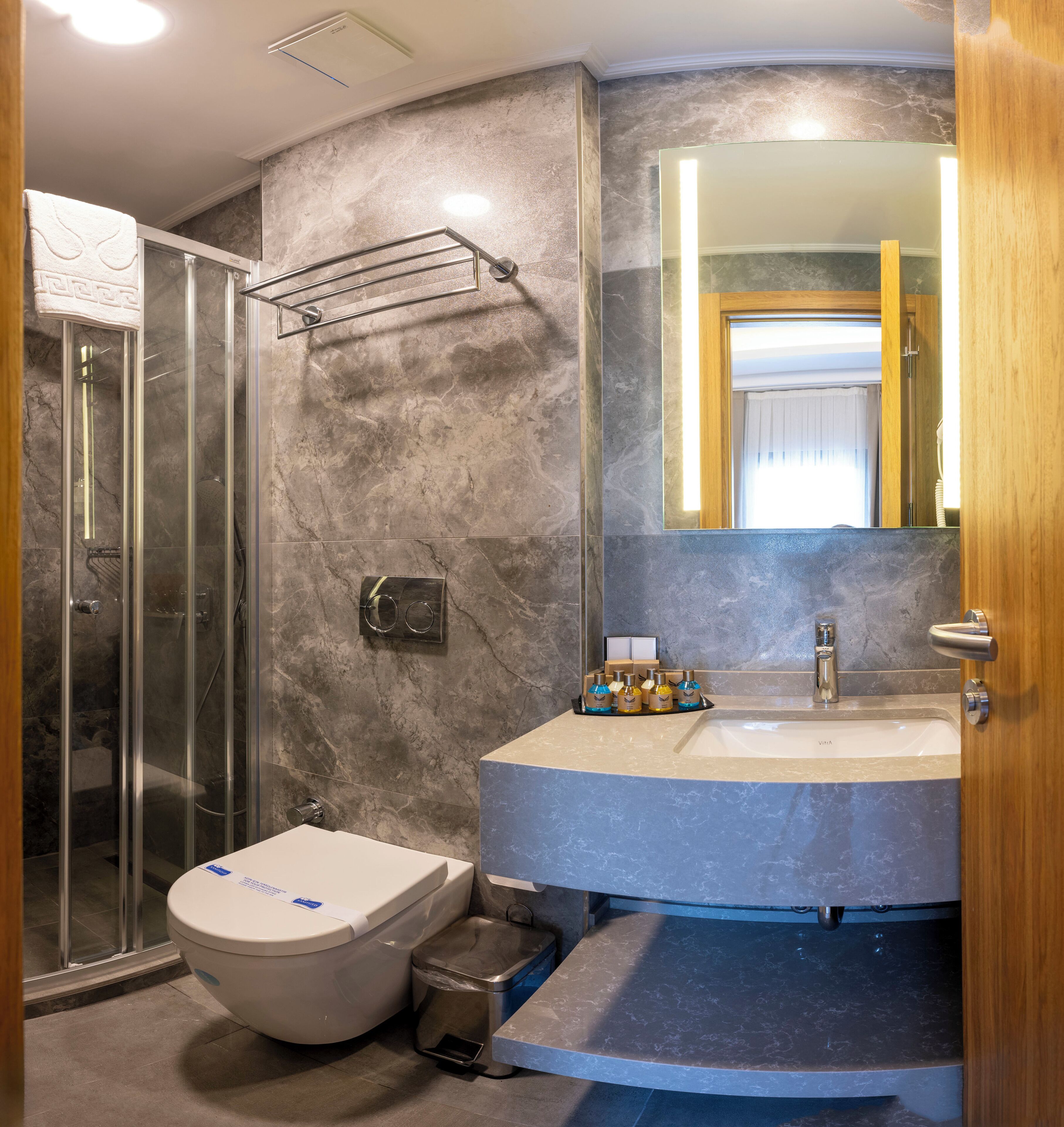 Een badkamer met een douchecabine van glas, een toilet, een wastafel met spiegel en toiletartikelen op de wastafel.