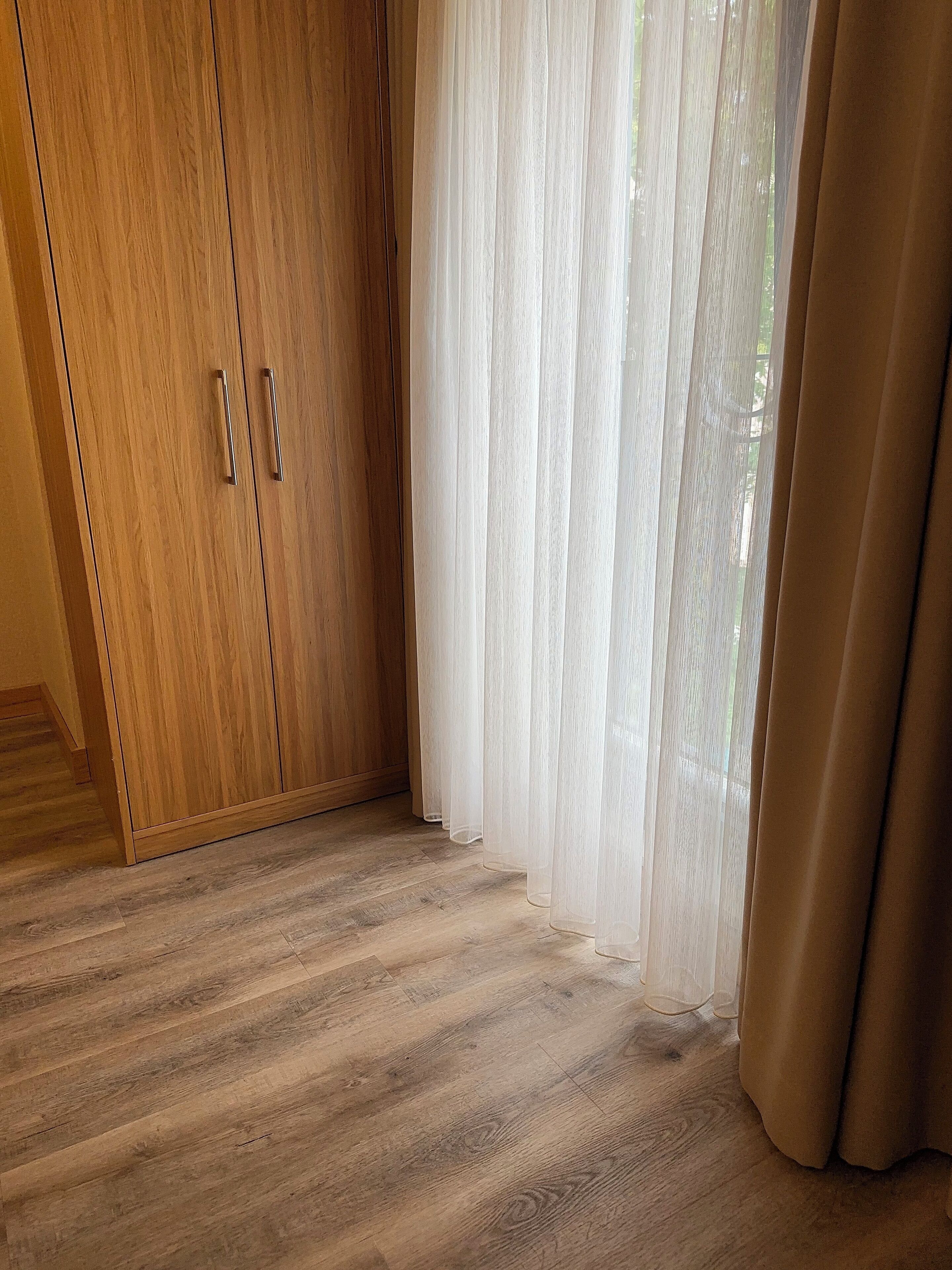 Ein Zimmer mit Holzschrank, durchsichtigen Vorhängen und Holzboden.