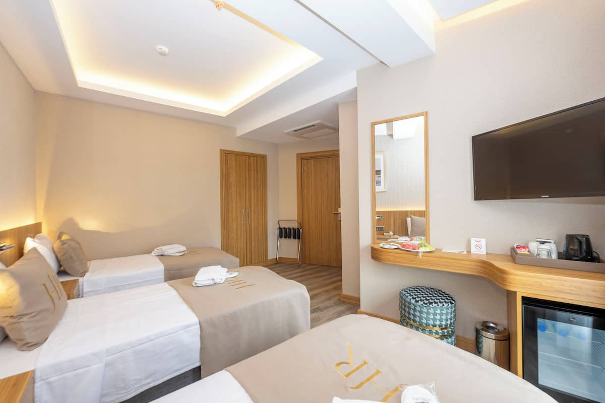 Habitación de hotel con dos camas, televisión, minibar y un pequeño cubo de basura.
