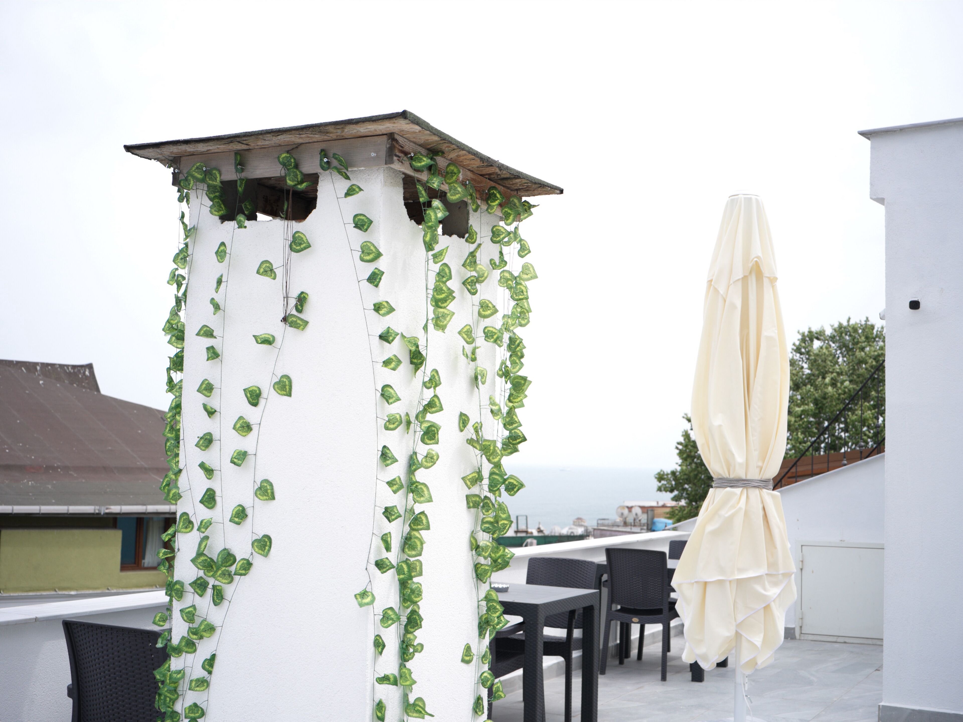 A rooftop terrace with a white column covered in green ivy, black wicker furniture, and a beige umbrella.