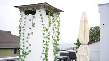 A rooftop terrace with a white column covered in green ivy, black wicker furniture, and a beige umbrella.