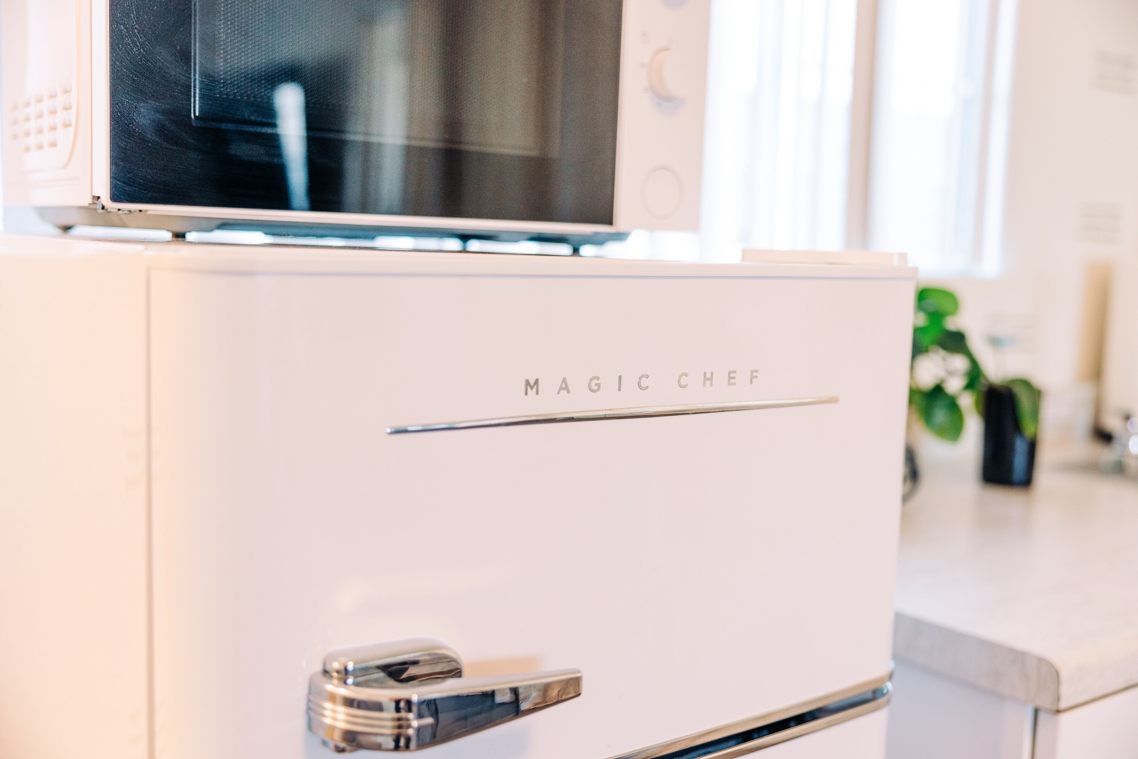 Cocina blanca con un microondas encima de un refrigerador blanco que dice "MAGIC CHEF".