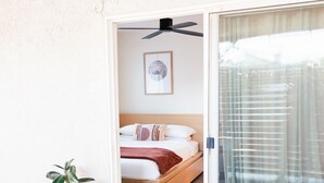 Ein Schlafzimmer mit Bett, Deckenventilator, Wandbild und einer Glastür mit Vorhang.