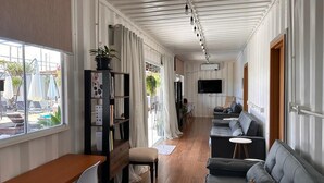 A modern living room with a wooden desk, a grey sofa, and a bookshelf. - Villela Stay - Villa Kubitschek - Country house Lago Sul Brasília-DF (Lago Sul)