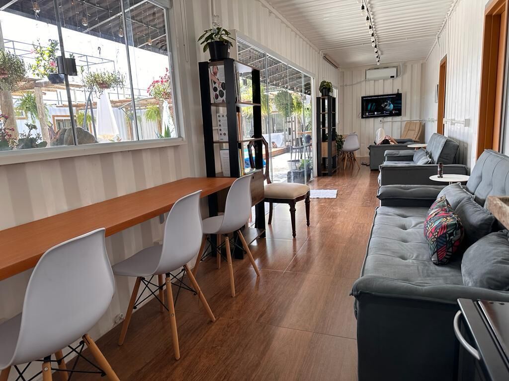 A modern interior with a wooden dining table, white chairs, a grey sofa, and a TV mounted on the wall.