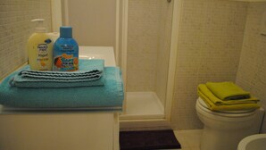 Ein Badezimmer mit einer weißen Badewanne, einer weißen Toilette und einer Duschkabine. Am Rand der Badewanne stehen zwei Shampooflaschen und eine Lotionflasche.