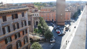 Straßenansicht mit einem markanten Turm, parkenden Autos und Gebäuden mit Balkonen.