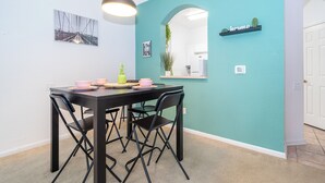 Un coin repas avec une table et des chaises noires, un luminaire suspendu et des murs de couleur turquoise.