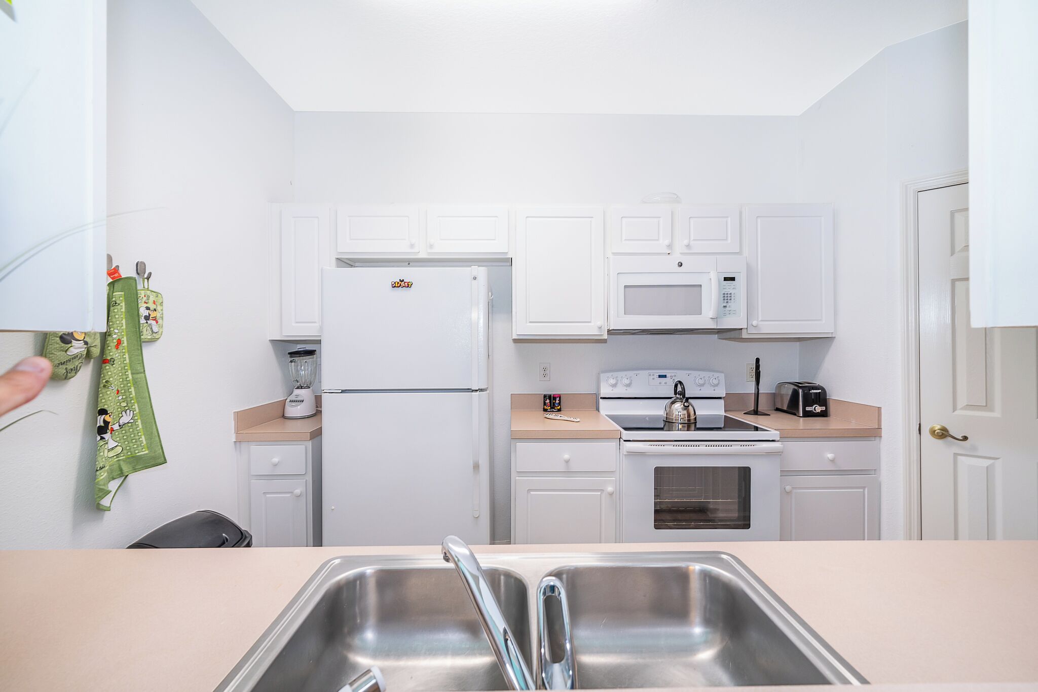 A compact kitchen with white cabinets, a refrigerator, a microwave, a stove, and a sink.