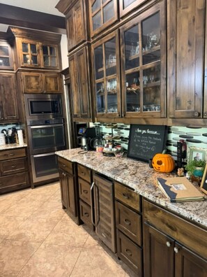 A kitchen with wooden cabinets, a granite countertop, and a chalkboard with writing.