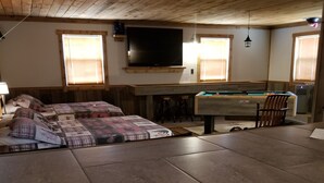 Una habitación acogedora con techo de madera, una cama grande con ropa de cama estampada, un televisor sobre la chimenea y una mesa de billar.