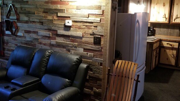 Una sala de estar acogedora con una pared de madera, un sofá de cuero negro, una mecedora de madera y una cocina al fondo.