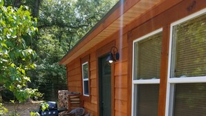 Una cabaña de madera con terraza, una parrilla y una silla.