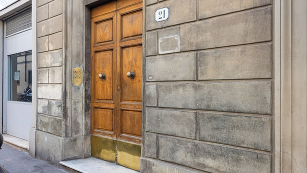 A wooden double door with a brass knocker, a number plaque, and a small step leading to the entrance. - Ognissanti Flat by Mmega (Florence)