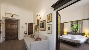 A hotel room with a bed, a sofa, a wooden door, and framed pictures on the wall. - Ognissanti Flat by Mmega (Florence)