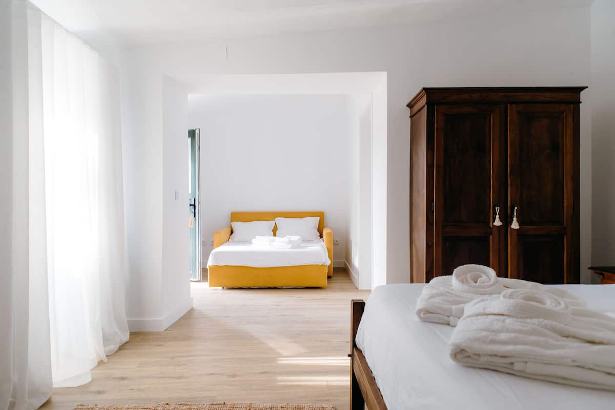 A hotel room with a bed, a wooden wardrobe, and a view of another room.