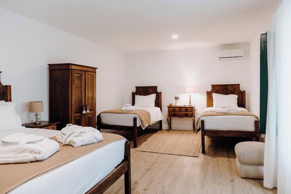 A hotel room with two single beds, a wooden wardrobe, a bedside table with a lamp, and a small table with a vase.