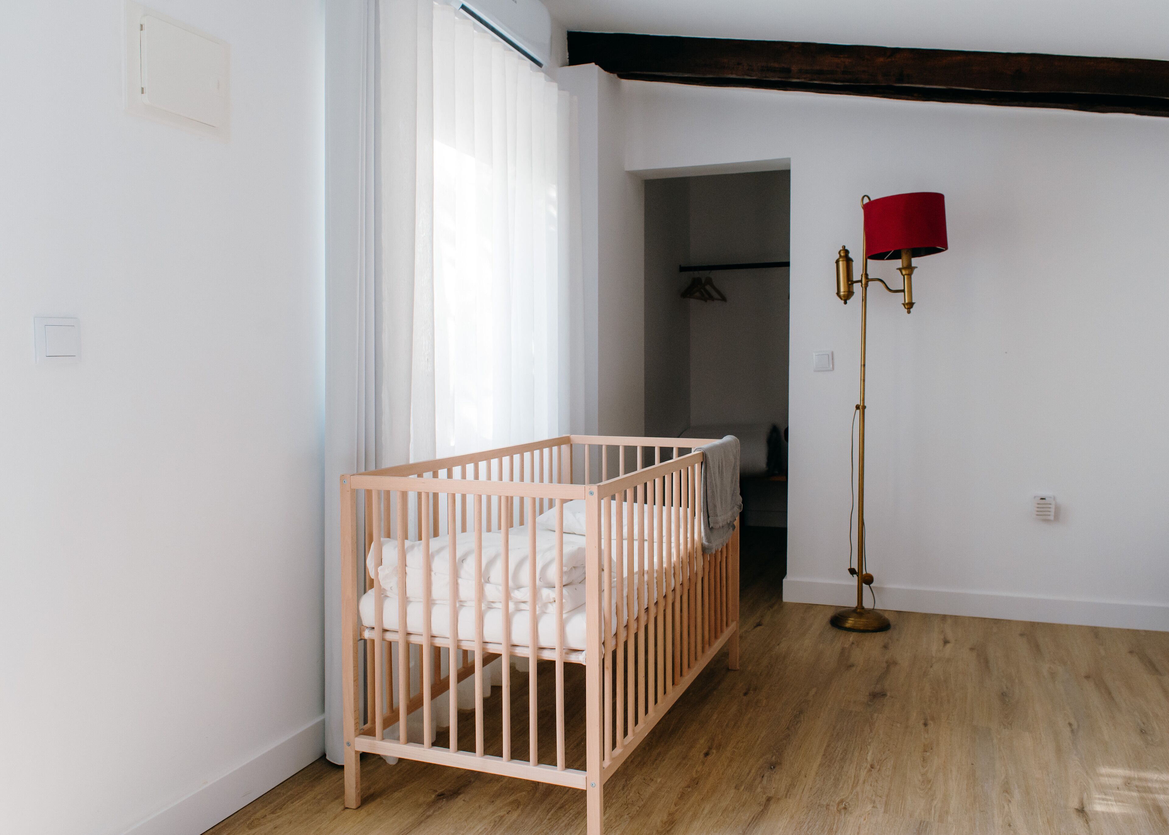 Een kamer met een houten wieg, een vloerlamp en een deur naar een andere ruimte.