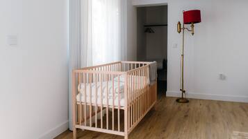 Een kamer met een houten wieg, een vloerlamp en een deur naar een andere ruimte.