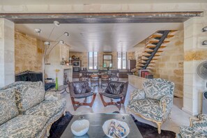A spacious living area with leather chairs, a sofa, a coffee table, and a staircase leading to an upper floor.