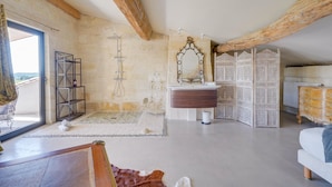 Une pièce spacieuse avec un plafond en bois, un grand miroir, une commode en bois et une vue sur l’extérieur, visible à travers une porte vitrée.