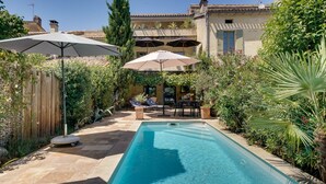 Une piscine dotée d’une terrasse en bois, entourée d’une végétation luxuriante et agrémentée d’un espace patio avec des parasols.