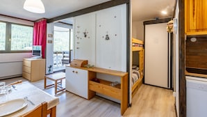 Une pièce de taille modeste comprenant un lit superposé, un bureau et un coin repas.
