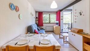 Un coin repas avec une table dressée pour quatre personnes, un canapé et un espace cuisine équipé d’un barbecue.