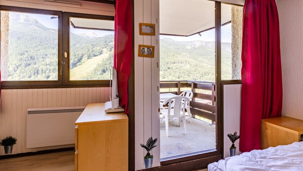 Une chambre avec un bureau en bois, un lit et un balcon offrant une vue sur les montagnes.