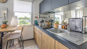 Eine moderne Küche mit einem großen Fenster, einem Essbereich mit Korbstühlen sowie diversen Küchenutensilien und Pflanzen.