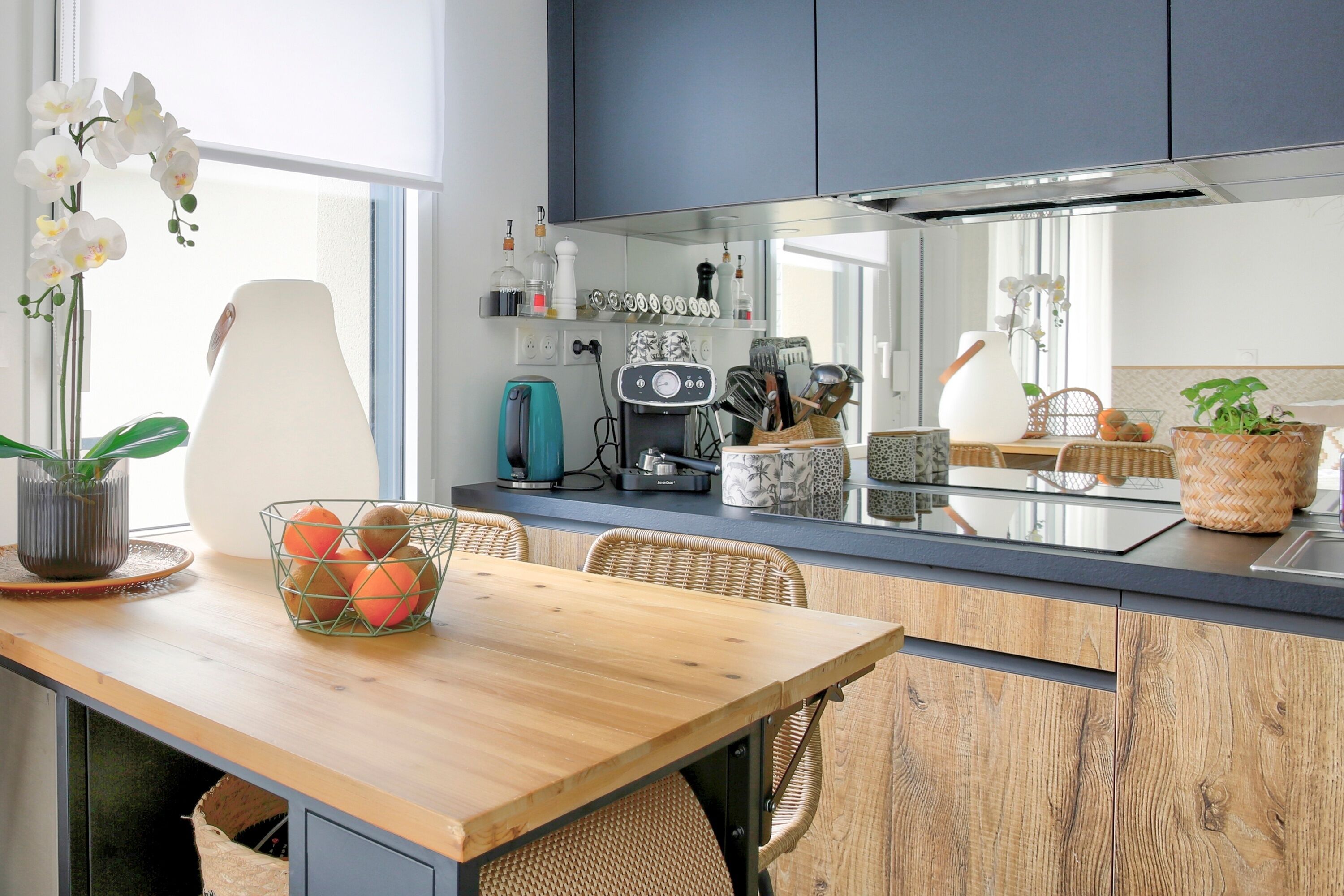 Een moderne keuken met een houten eettafel, rieten stoelen en diverse keukenapparaten en keukengerei.